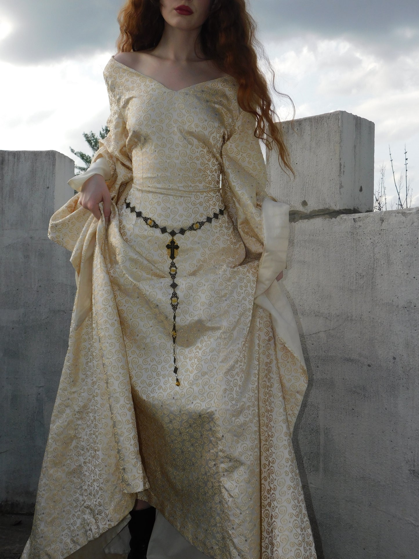 Close-up of 1930s Spanish silk gown highlighting gold embroidered pattern, draped sleeves, and ornate rosary belt.