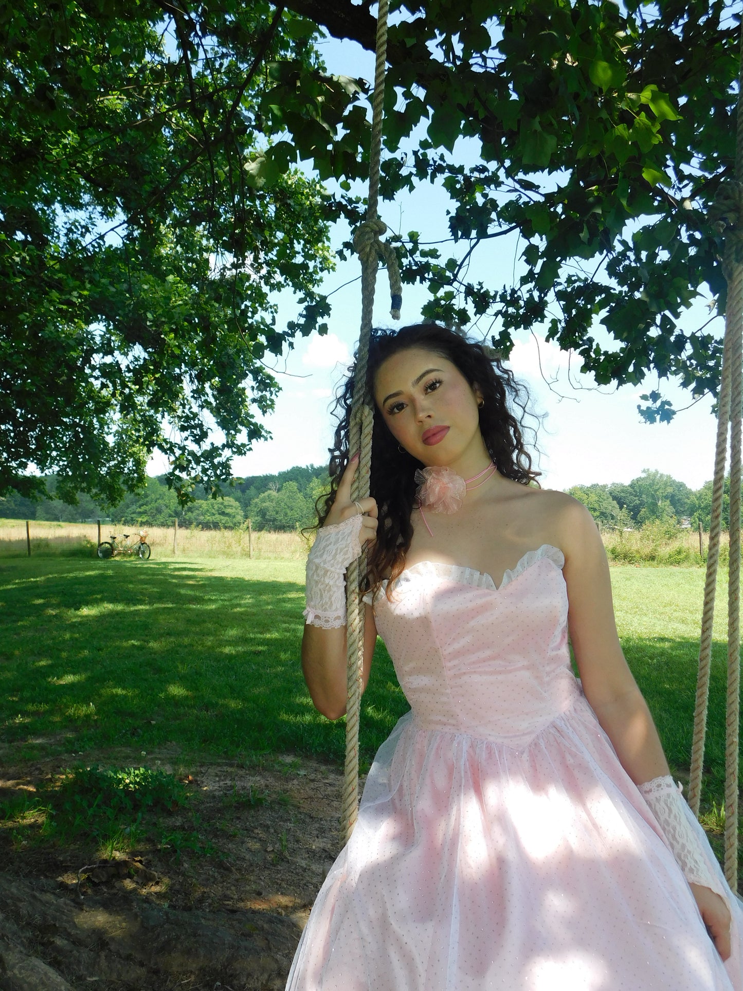 1980s blush pink Gunne Sax dress on model swinging under tree, styled with vintage gloves and floral neckpiece.