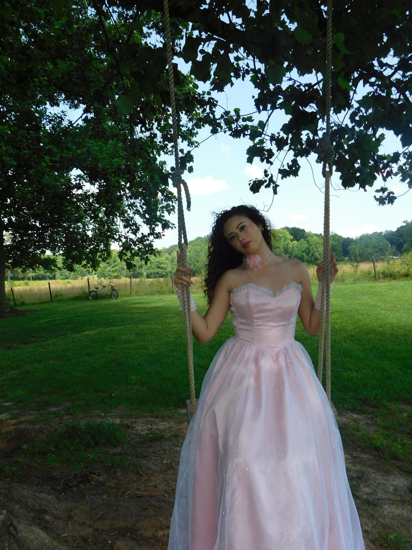 Model wearing 1980s Jessica McClintock Gunne Sax gown on rope swing, styled with gloves and floral choker in romantic countryside setting.