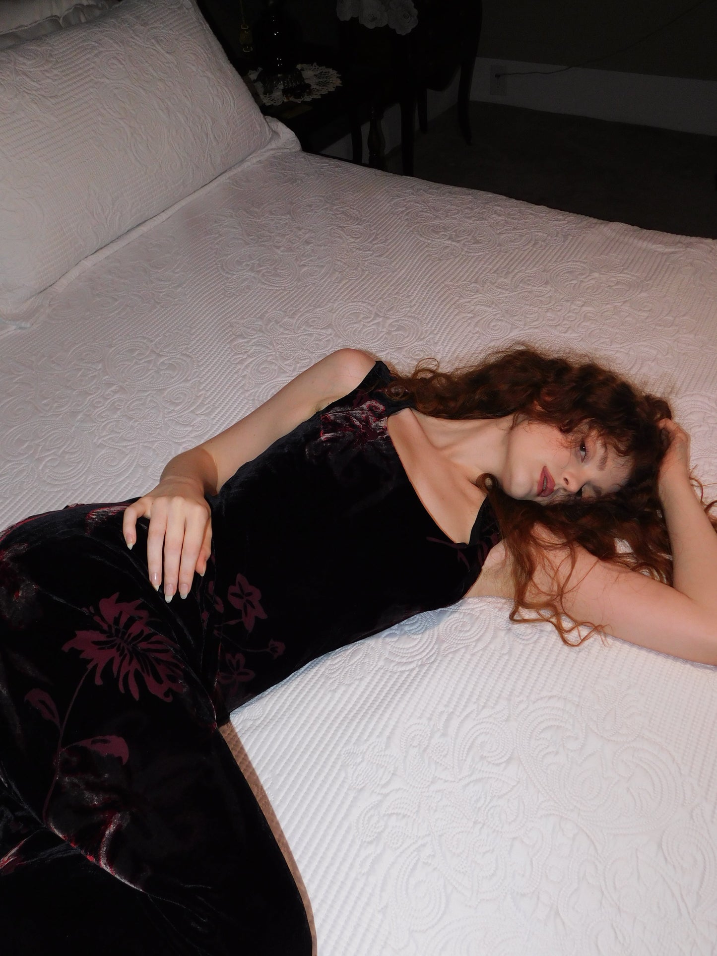 Vintage silk devoré velvet gown with deep burgundy floral motifs, model resting on textured white bed cover