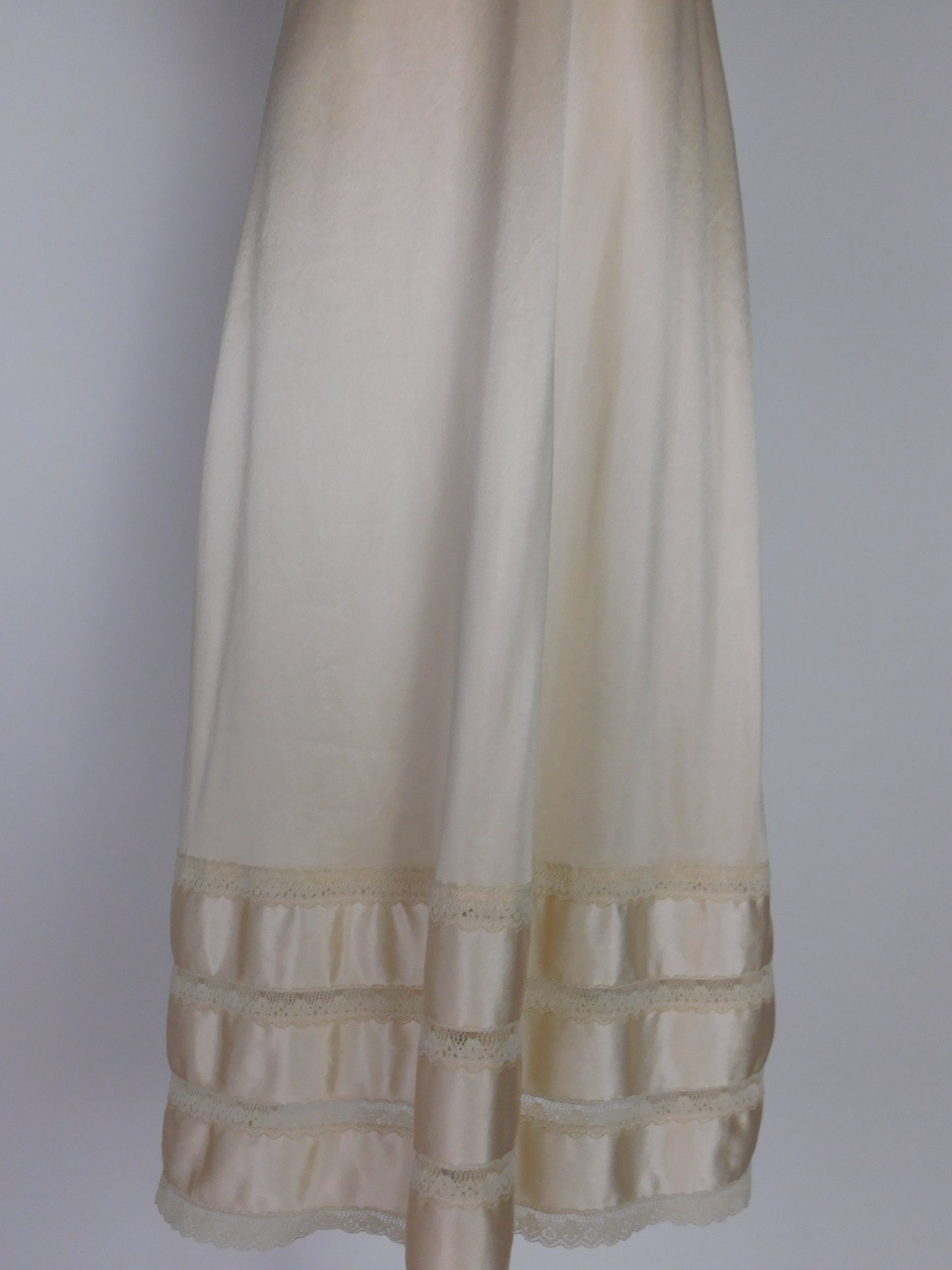 Lower half of vintage ivory satin slip dress from 1990s highlighting tiered lace trim and lustrous satin panels near hem