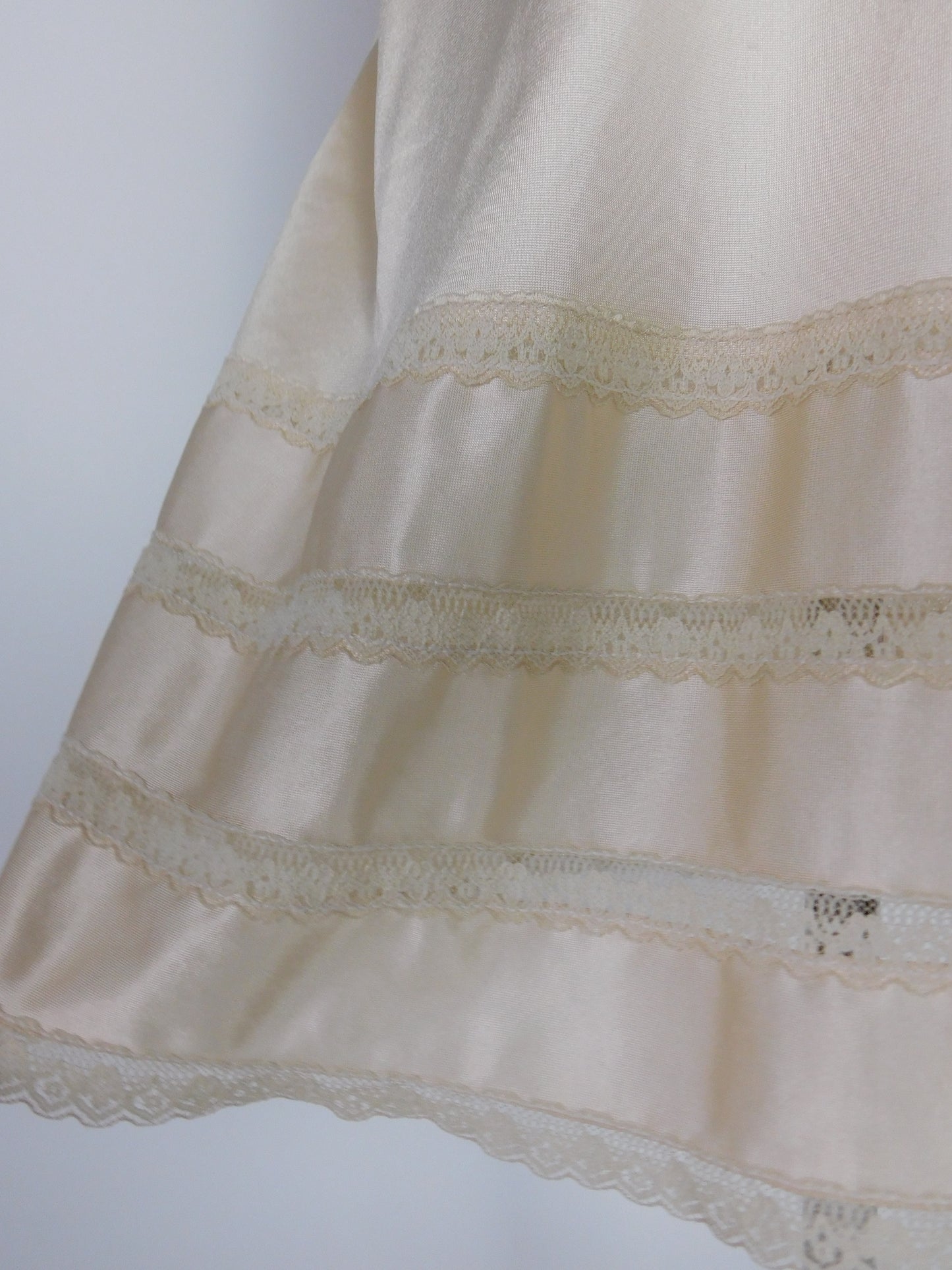 Detailed close-up of lace trim on 1990s ivory satin slip dress hem showing craftsmanship and vintage fabric texture