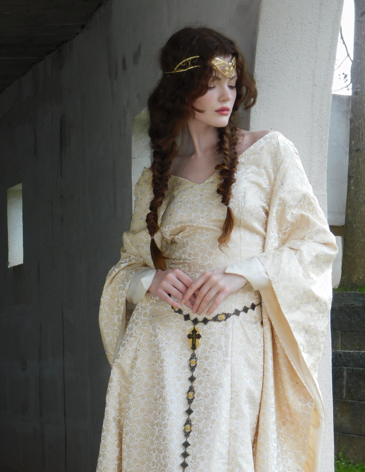 Woman with braided hair and gold crown wearing a 1930s Spanish silk gown in an arched hallway.