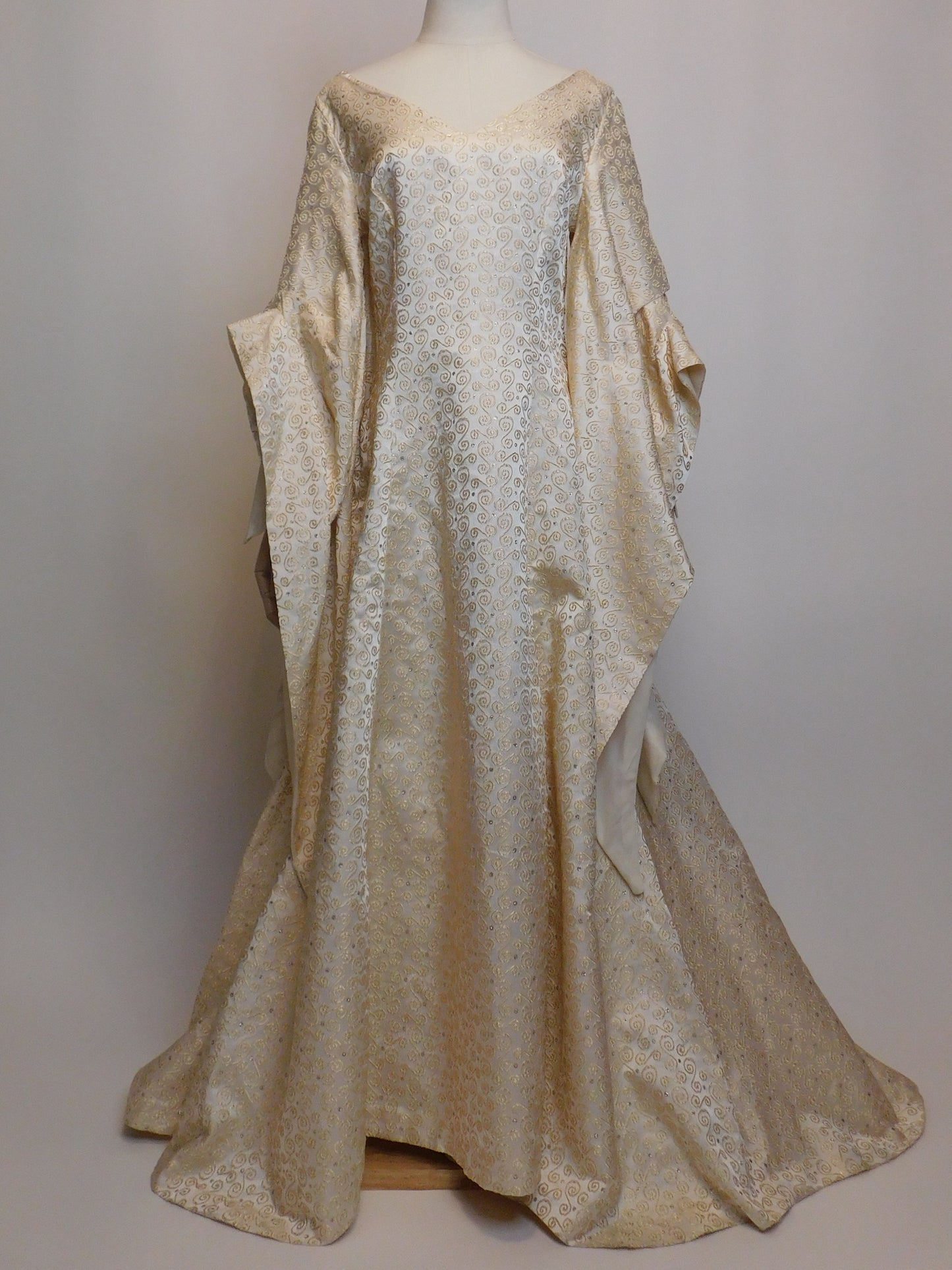 1930s Spanish silk gown displayed on a mannequin. Features long draped sleeves and a rich gold swirl embroidery on ivory silk.