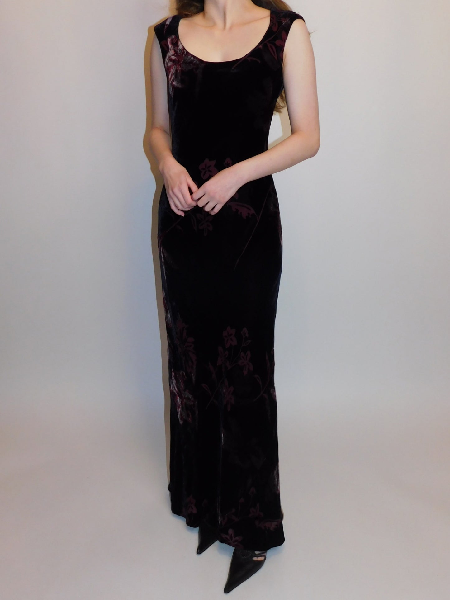 Angled view of long silk velvet floral gown with soft burgundy pattern, modeled with arms crossed at waist