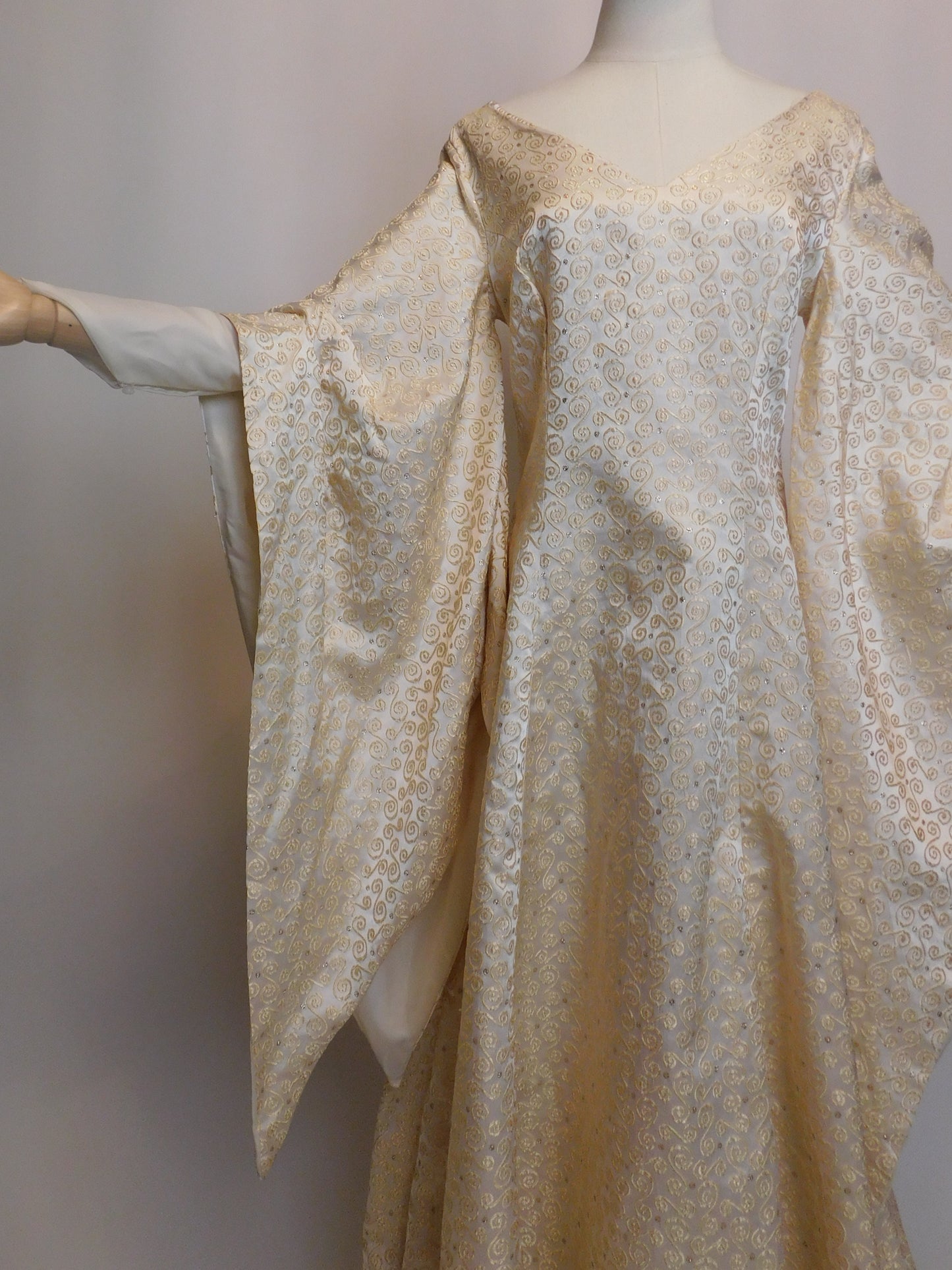 Close-up of the left half of the gown on a mannequin, highlighting the structured bodice, off-shoulder neckline, and elaborate gold embroidery on flowing silk sleeves.