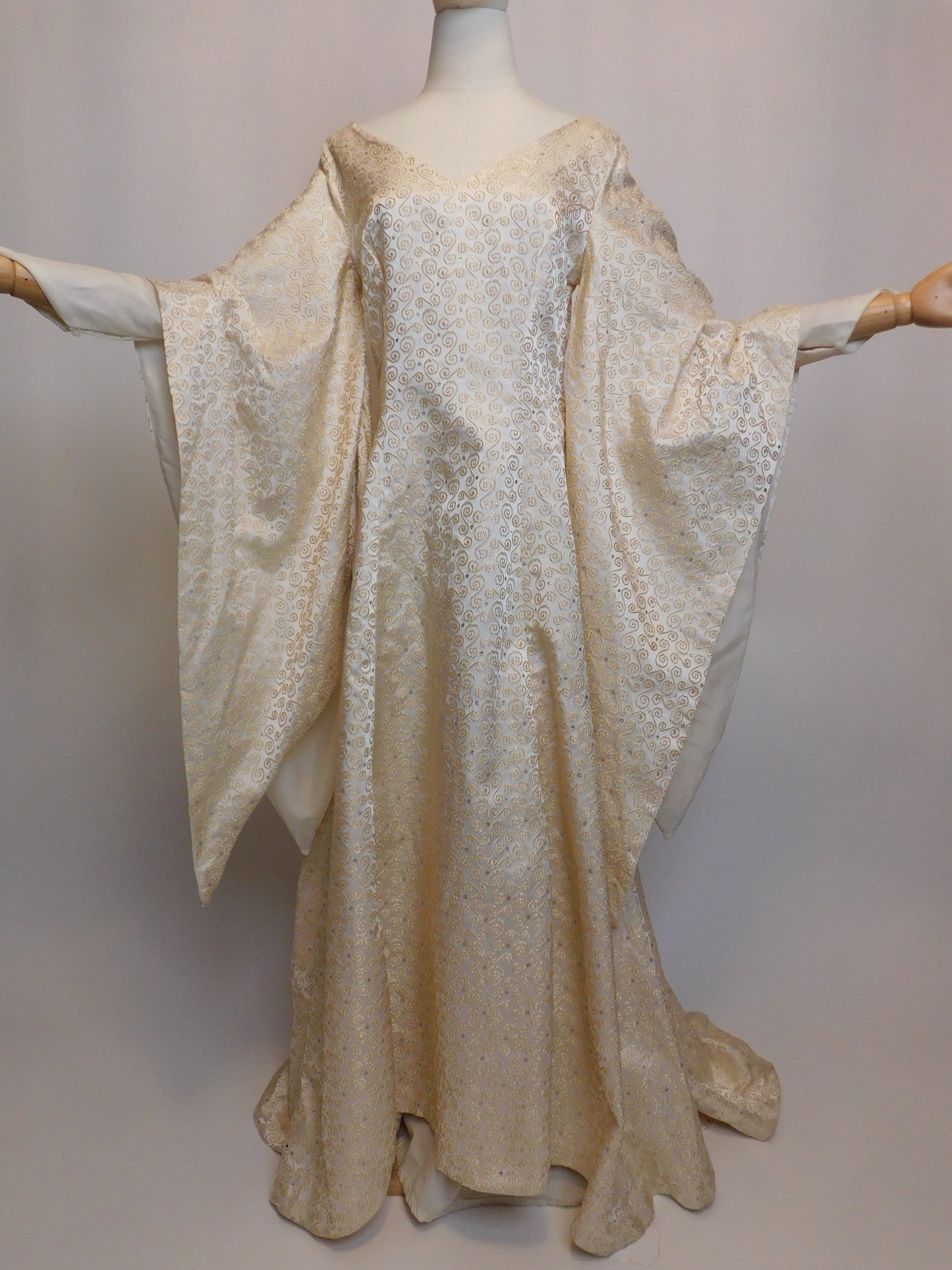 Front view of an antique 1930s Spanish silk gown displayed on a mannequin, with voluminous sleeves fully extended. The gown features intricate golden embroidery and a sweeping hemline.