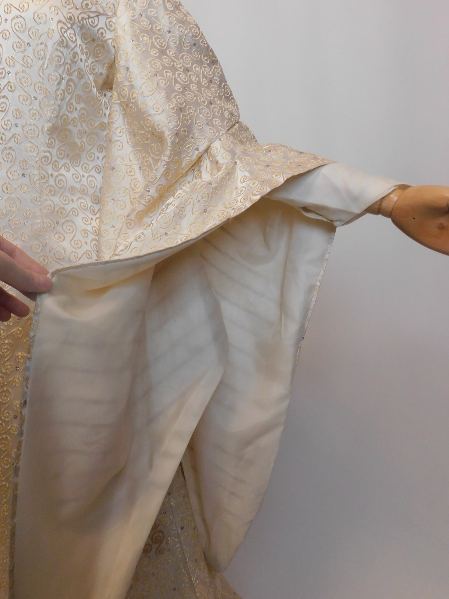 Detailed view of the interior of the sleeve being lifted to reveal the gown's luxurious ivory silk lining and delicate construction beneath the ornate outer embroidery.