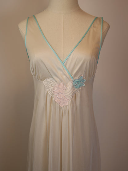 Close-up of 1970s vintage white satin slip dress showing pink and blue appliqué flowers and mint lace trim details