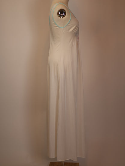 Side profile of 1970s white maxi slip dress with pastel appliqué, soft satin drape and delicate mint-trim straps