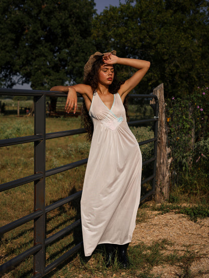 Vintage 1970s white maxi slip dress with pastel appliqué flowers, soft satin texture, styled rustic western chic outdoors