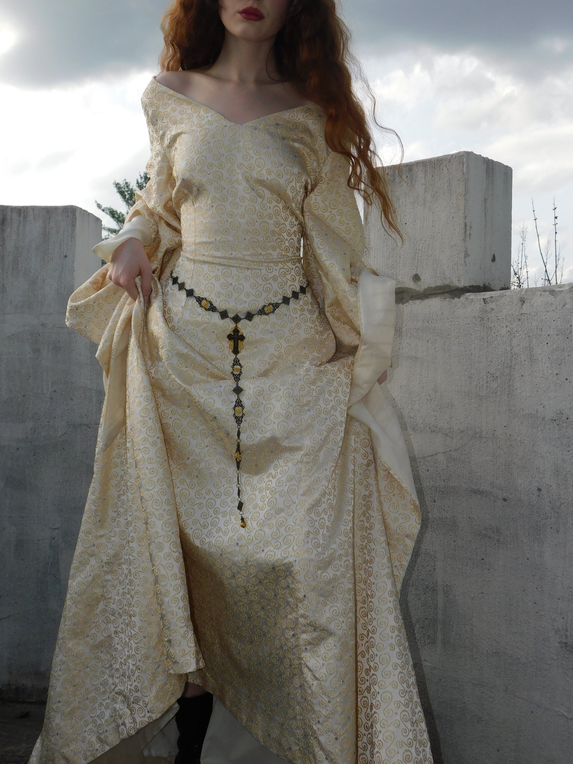 Close-up of 1930s Spanish silk gown highlighting gold embroidered pattern, draped sleeves, and ornate rosary belt.