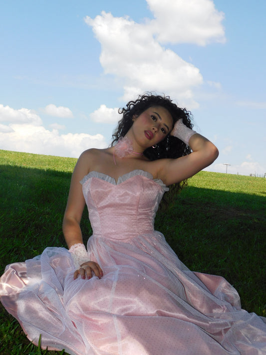 Model wearing 1980s Gunne Sax Jessica McClintock pink satin strapless lace gown reclining in grass under bright sky