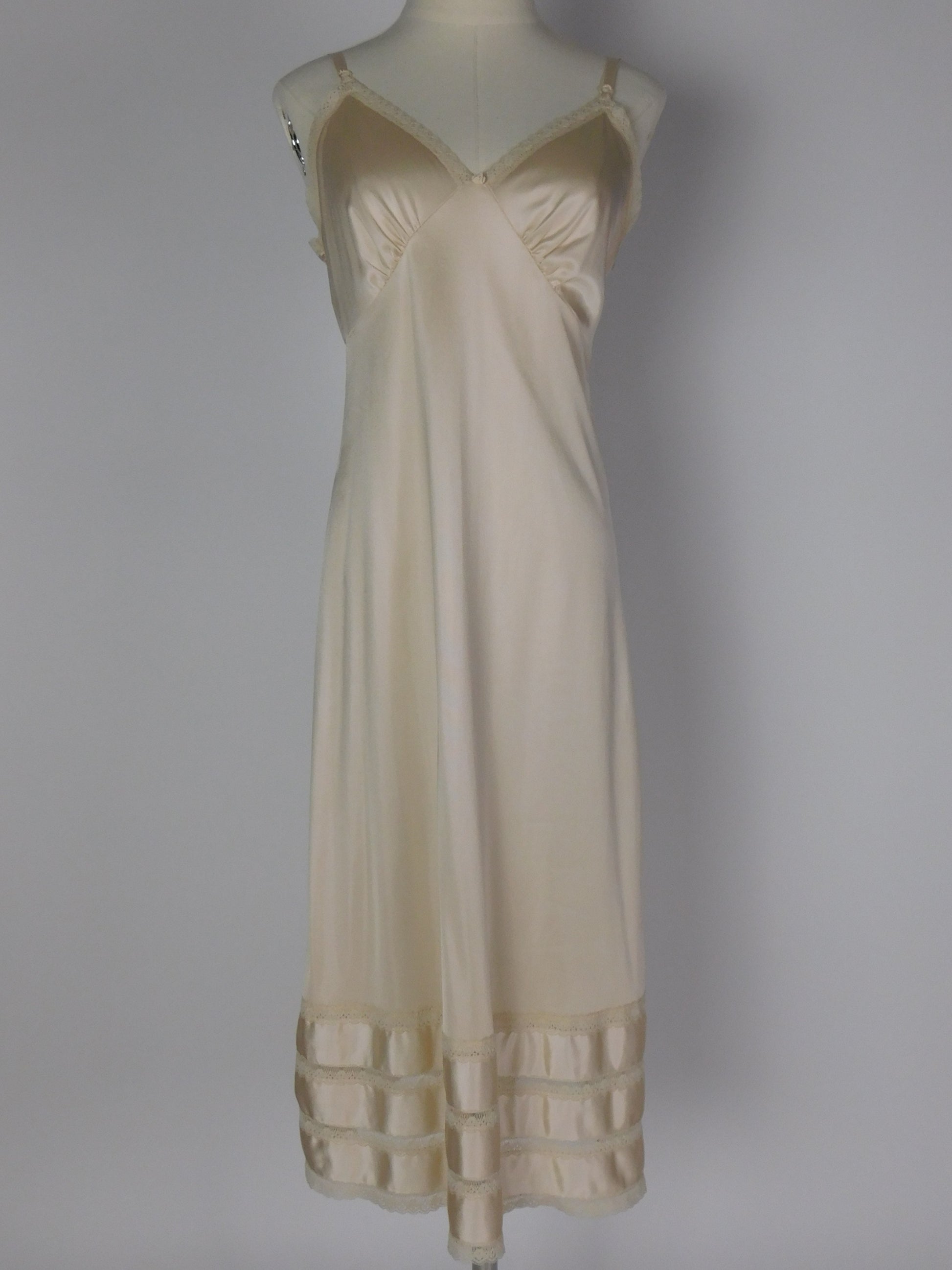 Full front view of 1990s ivory satin slip dress with lace trim, V neckline and silky bias cut on mannequin against neutral backdrop