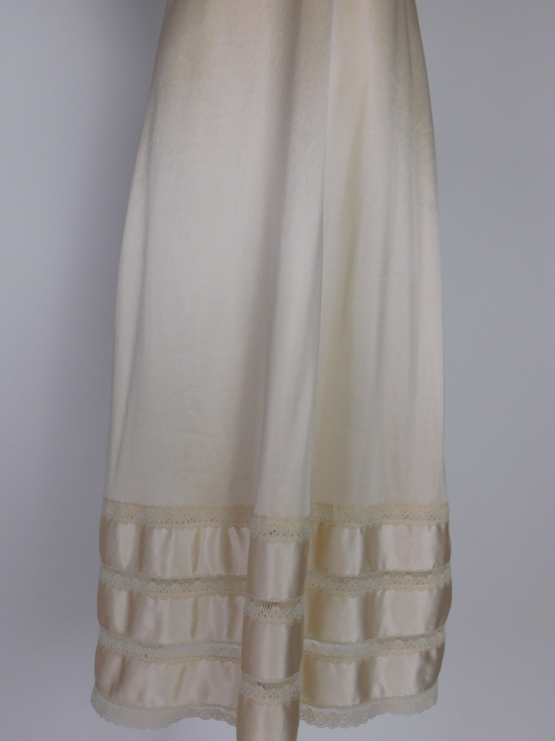 Lower half of vintage ivory satin slip dress from 1990s highlighting tiered lace trim and lustrous satin panels near hem