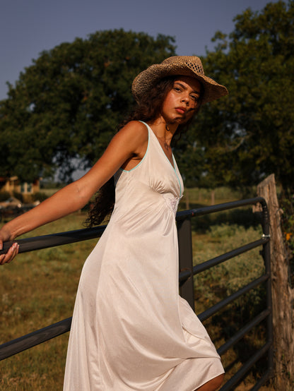 Side angle of 1970s vintage white maxi slip dress with pastel lace trim, flowy satin fabric under natural afternoon light