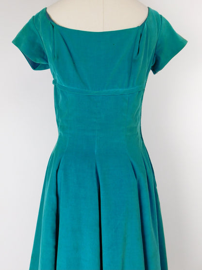 Back view of 1950s teal blue velvet midi dress on mannequin, featuring a fitted bodice and full pleated skirt with cap sleeves.