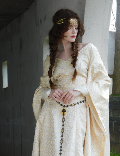 Woman with braided hair and gold crown wearing a 1930s Spanish silk gown in an arched hallway.