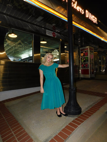 Full-length shot of model in blue velvet dress, leaning on a streetlamp outside a neon-lit diner