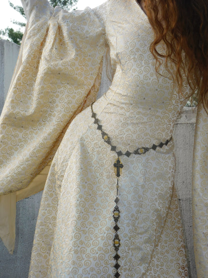 Close-up of 1930s Spanish silk gown featuring delicate swirling gold motifs and a vintage cross belt.