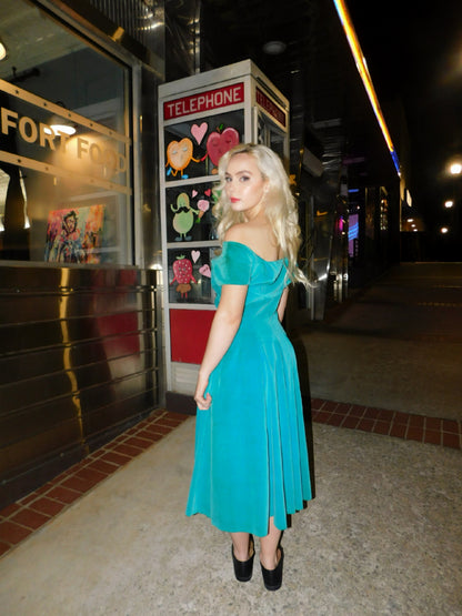 Back view of model in off-the-shoulder 1950s velvet dress, standing in front of a retro phone booth